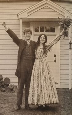 a man and woman are standing in front of a house with their arms outstretched up