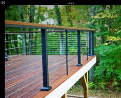 a wooden deck with metal railings in front of some trees and bushes on the other side