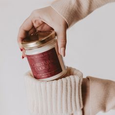 a person holding a jar of christmas cookies in their hand and wearing a white sweater