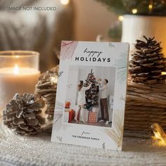 a christmas card sitting on top of a table next to some pine cones and candles