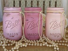 three pink mason jars sitting on top of a table next to pearls and a bead necklace