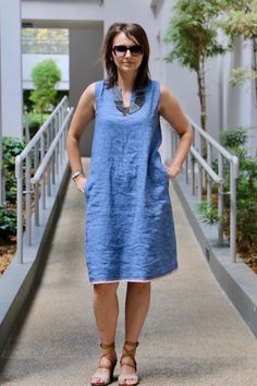 a woman standing on a walkway wearing sunglasses and a blue dress