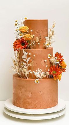 a three tiered cake decorated with flowers and leaves on top of two plates in front of a white wall