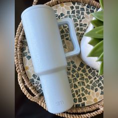 a white cup sitting on top of a wicker basket next to a potted plant