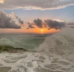 the sun is setting over the ocean with waves crashing in front of it and some clouds