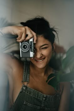 a woman holding an old fashioned camera up to her face and smiling at the camera