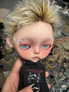 a close up of a person holding a doll with blonde hair and piercings on