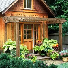 a small wooden house with potted plants in the front yard and an arbor attached to it