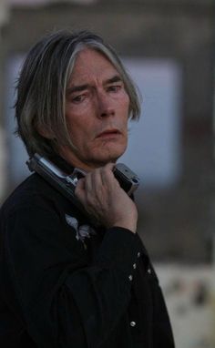 an older man with grey hair is talking on his cell phone while standing in front of a building