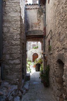 an alley way with stone buildings and potted plants on either side, leading into the distance