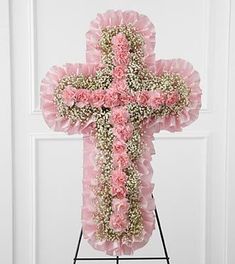 a cross made out of pink flowers on top of a stand