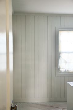 an empty bathroom with white walls and wood paneling on the wall, along with a window