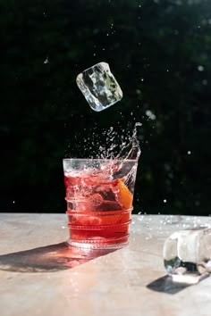 a glass filled with water and an orange wedged into the ice on top of a table