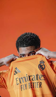 a man holding up a soccer jersey in front of an orange background with the words emirates flybetter printed on it