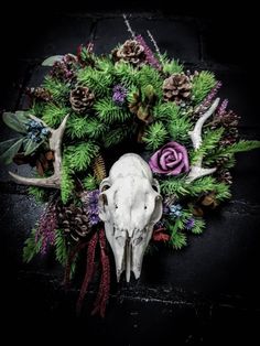 a deer skull is surrounded by pine cones and flowers on a black background with greenery