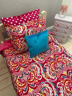 a bed with colorful sheets and pillows on top of it next to a night stand