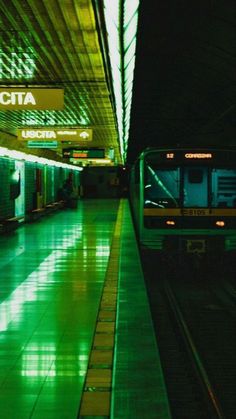 an empty subway station at night with green lights on the platform and people waiting to board