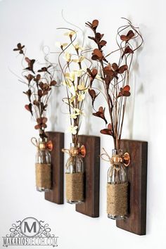 three vases with flowers in them are hanging on the wall and one is filled with sand