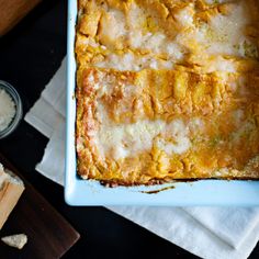 a square casserole dish with cheese and bread on the table next to it