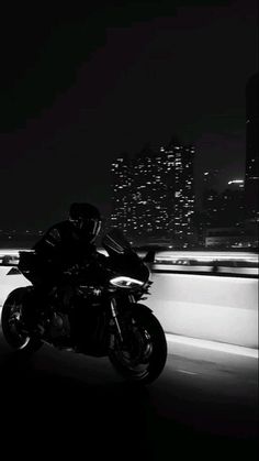 black and white photograph of a person riding a motorcycle in the city at night time