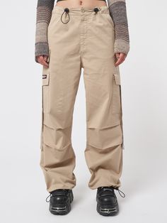 Arm yourself with ’90s and noughties attitude! Take a look at our cargo parachute pants in beige, featuring a baggy fit, utility pockets and adjustable toggle waist and hems. Find y2k pants, retro trousers & more aesthetic clothes at Minga London. Tech Cargo Pants, Jeans With Chains, Retro Trousers, Parachute Cargo Pants, 90s Pants, Denim Button Skirt, Minga London, Parachute Cargo, Y2k Pants