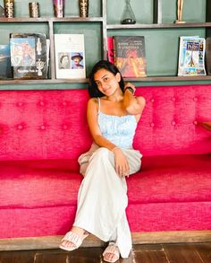 a woman sitting on top of a pink couch in front of a book shelf filled with books