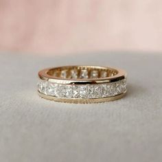 a wedding band with princess cut diamonds on it, sitting on top of a white cloth