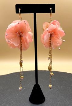 two pink flowers with chains hanging from them on a black display stand in front of a beige background