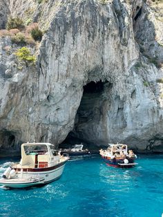 two boats are in the water near a cave