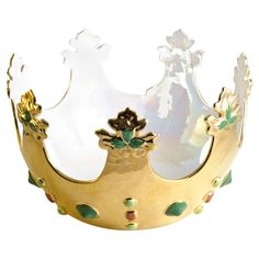 a gold crown with green leaves and flowers on it's sides, against a white background