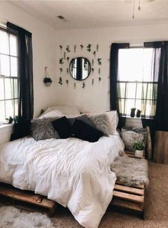 a white bed sitting under two windows next to a window filled with lots of pillows