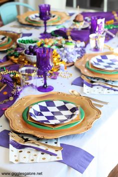 the table is set with purple and gold plates, napkins, and place settings