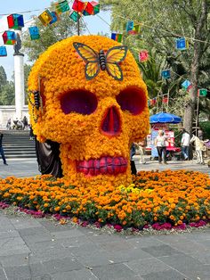 there is a large orange flower skull in the middle of a garden with people walking around it