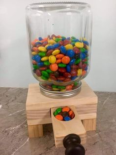 a glass jar filled with lots of candy sitting on top of a wooden block next to a