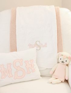 a white couch with two pillows and a stuffed animal on it's side next to a personalized blanket