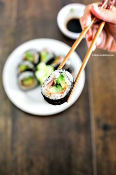 someone holding chopsticks over a plate of sushi