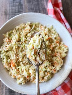 a white bowl filled with coleslaw and a spoon on top of a checkered table cloth