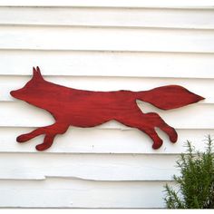 a metal red fox on the side of a white house with plants in front of it