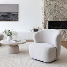 a living room with two chairs and a table in front of a stone fire place