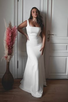 a woman in a white dress standing next to a vase