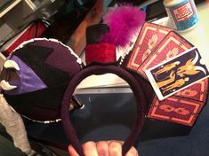 a hand is holding up a mickey mouse ears headband with cards and other items around it