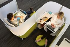 two people sitting at desks with laptops on their laps and one person reading