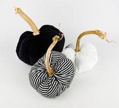 three black and white pumpkins sitting side by side on a white surface with gold stems