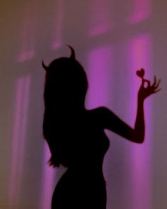 the silhouette of a woman holding a rose in her right hand and wearing devil horns