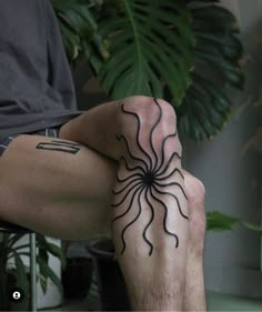 a man's legs with an intricate tattoo on his left leg, sitting in front of a potted plant