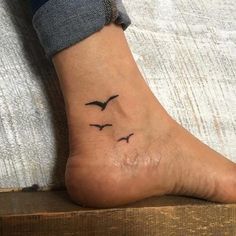 a small black bird tattoo on the right foot, with two birds flying above it