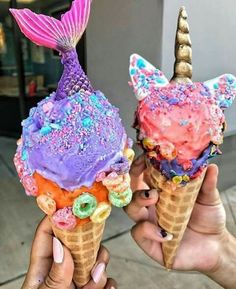 two ice cream cones with colorful toppings on them, being held up by someone's hand