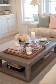 a coffee table with candles, books and flowers on it in front of a couch