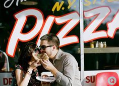 a man and woman sharing a piece of pizza in front of a restaurant window,