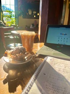 a laptop computer sitting on top of a wooden table next to a plate of food